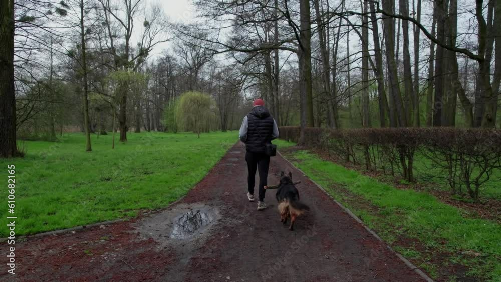 A man with his dog takes a walk in the park on a spring day, wearing a cap and a vest, the sky is cloudy. A man with his dog takes a walk in the park on a spring day, wearing a cap and a vest, the sky is cloudy.
