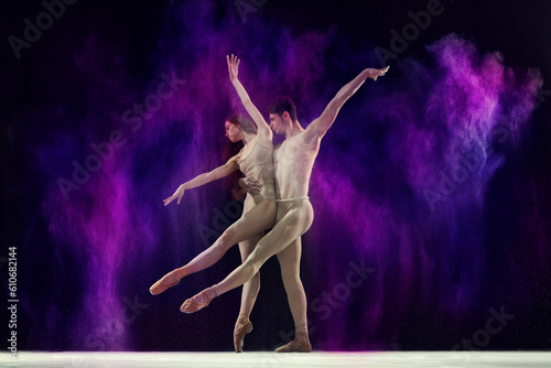 Beautiful, artistic young man and woman, professional ballet dancers performing with colorful powder splashes over black studio background. Art, festival, beauty of dance, inspiration, youth concept