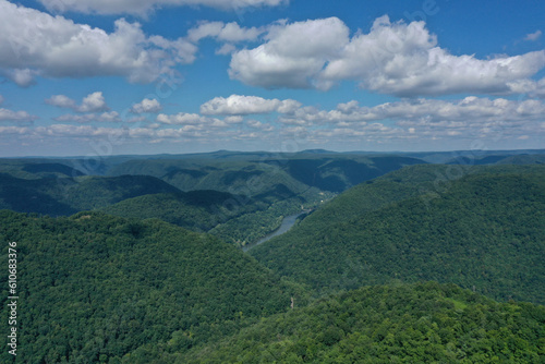River Cutting Through Green Mountains under a Blue Sky with Puffy White Clouds