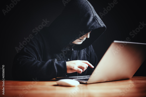 Black hood hacker in hood using tablet on desk to hacking privacy sensitive data cyber crime hack in dark room background matrix binary code. Cyber security cyber crime concept. Hacking phishing
