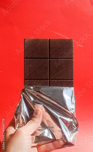 A person holding a dark chocolate bar in a red background 