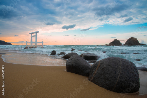 The sun setting on the horizon of beach where a white Shinto torii gate Sakurai Futamigaura's sacred Couple Stones view in Itoshima, Fukuoka, Japan scenic landscape