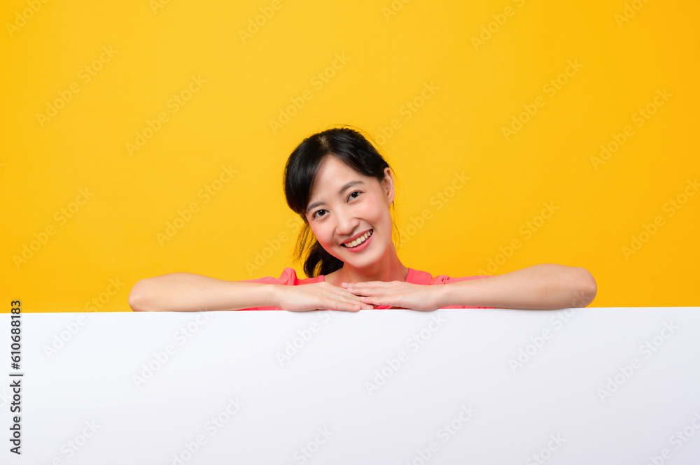 young asian sports fitness woman happy smile wearing pink sportswear standing behind the white blank banner or empty space advertisement board against yellow background. wellbeing lifestyle concept. young asian sports fitness woman happy smile wearing pink sportswear standing behind the white blank banner or empty space advertisement board against yellow background. wellbeing lifestyle concept.