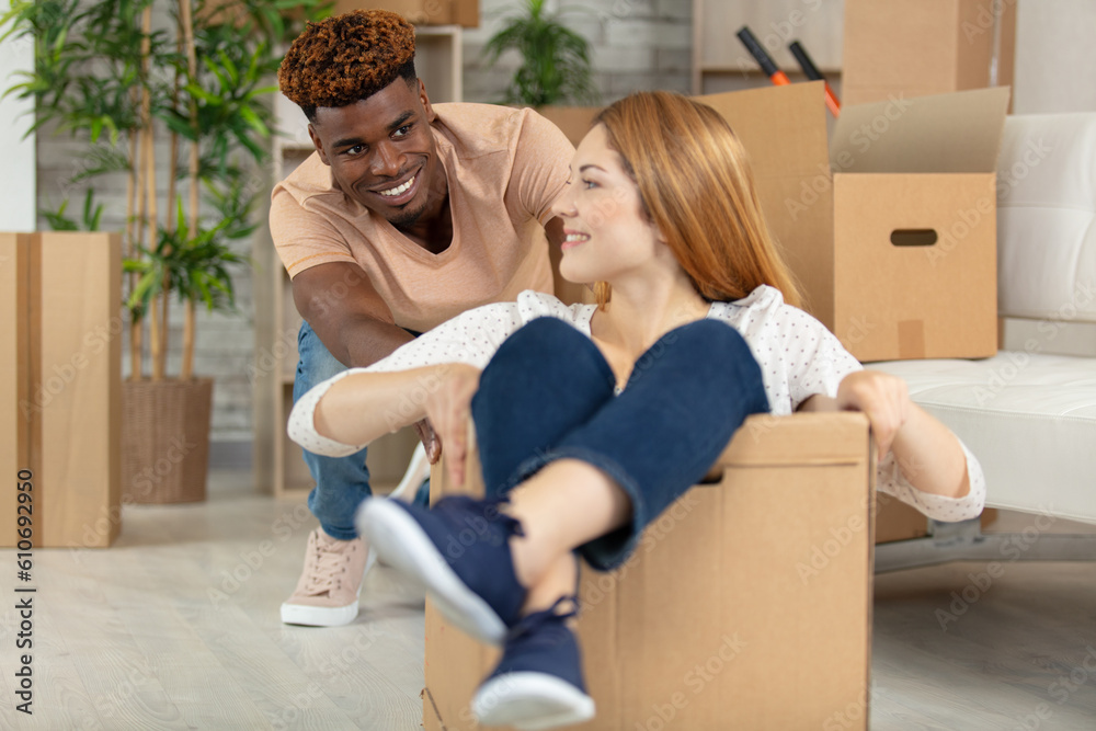 happy young man pushing the woman sitting on cardboard box happy young man pushing the woman sitting on cardboard box