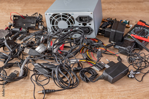 Pile of old wires, connections, headphones and chargers on a wooden table close-up. Replacement of old elements and parts of electronic devices. Repair of broken electronic devices and their elements