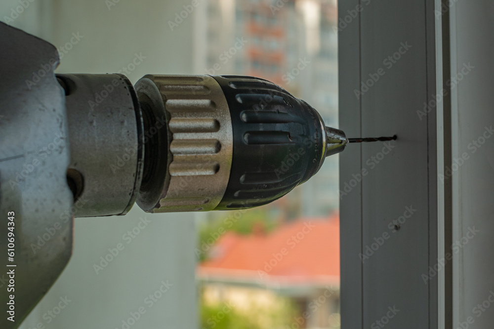 Worker drills holes in plastic window frame with electric drill. An