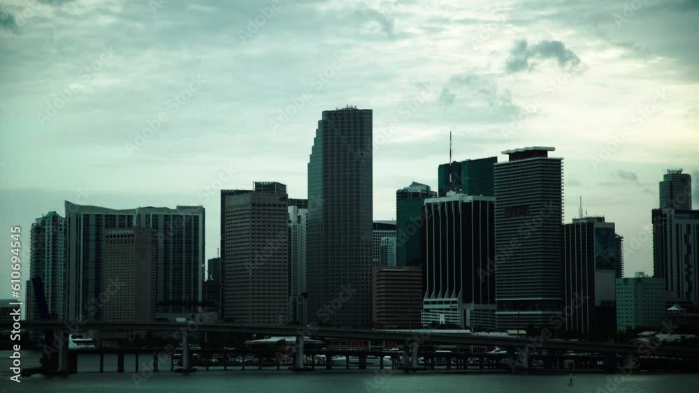 Lockdown Shot Of Vehicles On Bridge Over Sea Near Modern Buildings In City Against Cloudy Sky At Dusk - Miami, Florida Lockdown Shot Of Vehicles On Bridge Over Sea Near Modern Buildings In City Against Cloudy Sky At Dusk - Miami, Florida