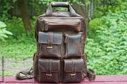 modern comfortable classic brown leather backpack with iron fittings stands on a brown wooden table outdoors during the day