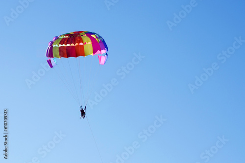 Tourists fly on a bright paraglider against the blue sky in the summer on a sunny day. Beach holidays, tourist marine entertainment