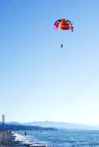 Tourists fly on a bright paraglider behind a boat over the sea against a blue sky in the summer on a sunny day. Beach holidays, tourist marine entertainment