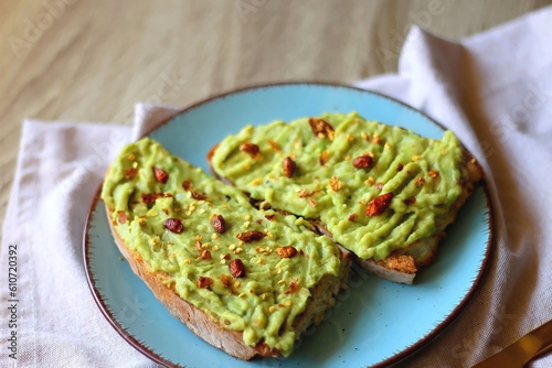 Turquoise plate with two pieces of avocado toast on wooden table. Selective focus.