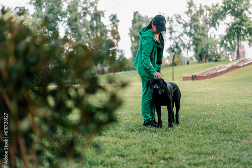 a woman trains a black dog of a large Cane Corso breed on a walk in the park praises and strokes her pet