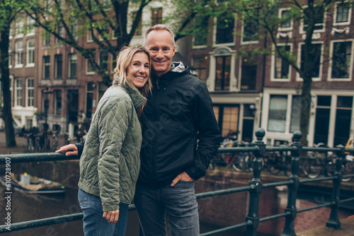 Photography Smiling middle age couple on bridge over rainy canal in Amsterdam boats, trees,