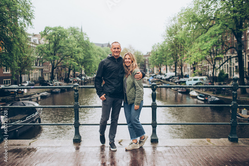 Canvas Print Smiling middle age couple on bridge over rainy canal in Amsterdam boats, trees,