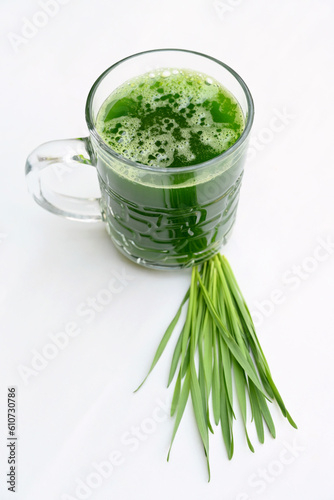 closeup the sliced green ripe wheat grass juice in the glass with wheat grass leaves on the white background.