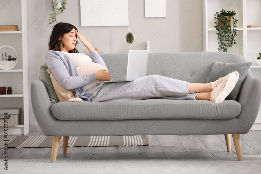 Tired young pregnant woman working with laptop on sofa at home Tired young pregnant woman working with laptop on sofa at home