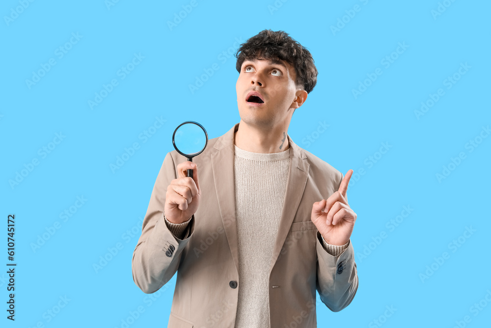 Young man with magnifier pointing at something on blue background Young man with magnifier pointing at something on blue background
