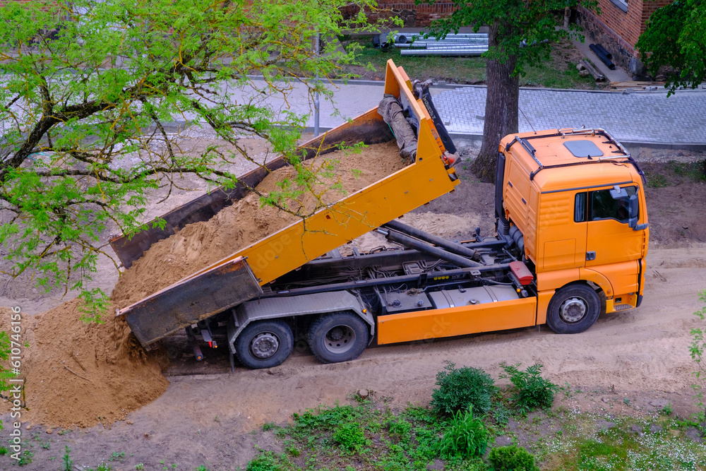 A large orange dump truck unloads the sand. A large orange dump truck unloads the sand.