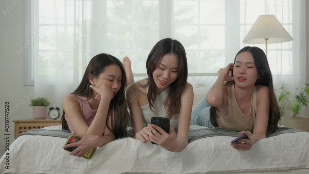 Group of Excited Asian young adults lying on bed using smartphones Group of Excited Asian young adults lying on bed using smartphones