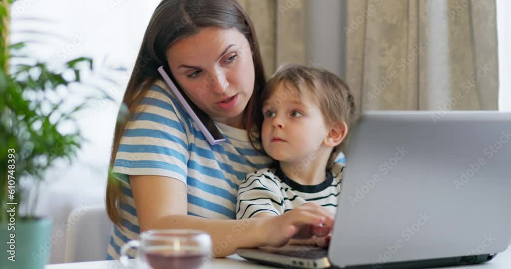 Mother working on laptop from home remotely with little son in her arms. Mother working on laptop from home remotely with little son in her arms.
