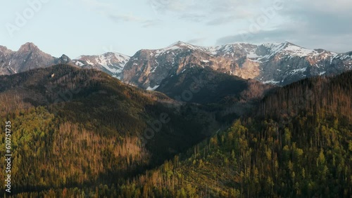 Epic view high mountain peaks covered with snow lit with warm sunrise or sunset light, aerial drone shot of beautiful mountains and green hills, spring season early morning, mountain range golden hour