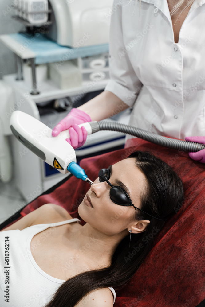Naklejka premium Laser removal of blood vessels on face of girl in dermatological clinic. Cosmetologist cleans face of girl from pigmentation using laser. Hardware treatment.
