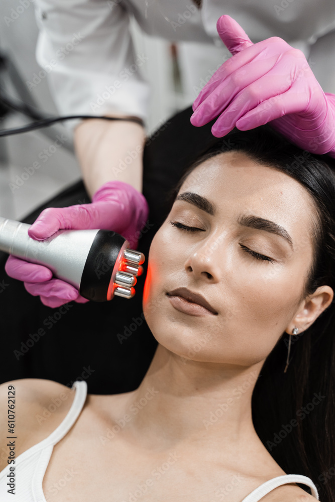 Radio frequency lifting with red light for young woman close-up. Dermatologist is doing radio frequency RF skin tightening. RF facelift firms and lifts sagging skin. Radio frequency lifting with red light for young woman close-up. Dermatologist is doing radio frequency RF skin tightening. RF facelift firms and lifts sagging skin.