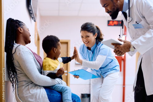 Happy nurse gives high-five to small black boy at medical clinic. photo