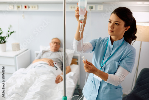 Nurse practitioner checking IV drip of senior patient at hospital ward.