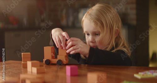 Busy game on the table performed by cute baby girl, orange wooden toy blocks, shy autistic child plays alone, builds street with houses. Mental disorder, domestic background. High quality 4K footage