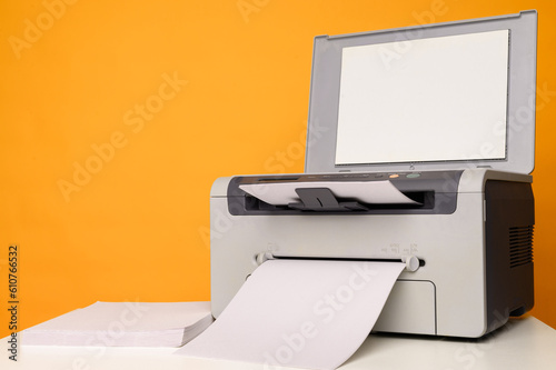 Front view of a multifunction device - printer, copier, scanner and a blank sheet of A4 paper on a white table