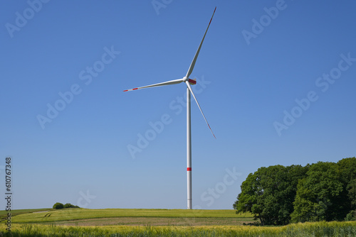 Tall wind turbine with a slender tower and three rotor blades standing on a field in a rural landscape against the blue sky, renewable energy concept, copy space photo