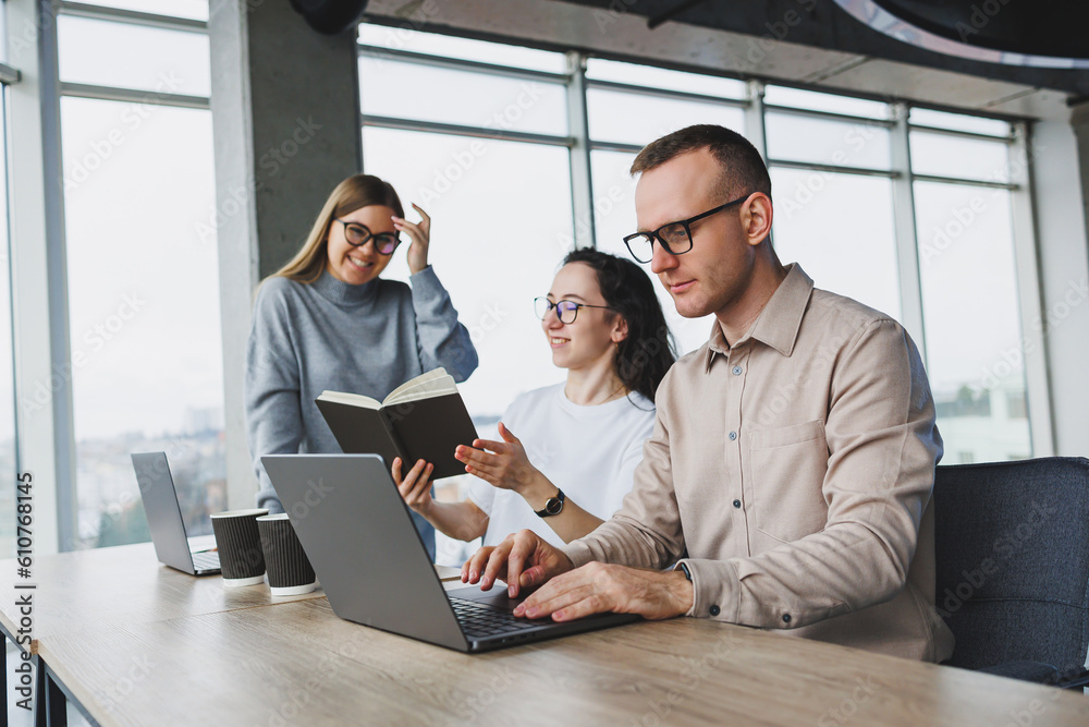 Naklejka premium Workflow in an office with large windows, colleagues working on a new project using a portable laptop. Modern office with employees.