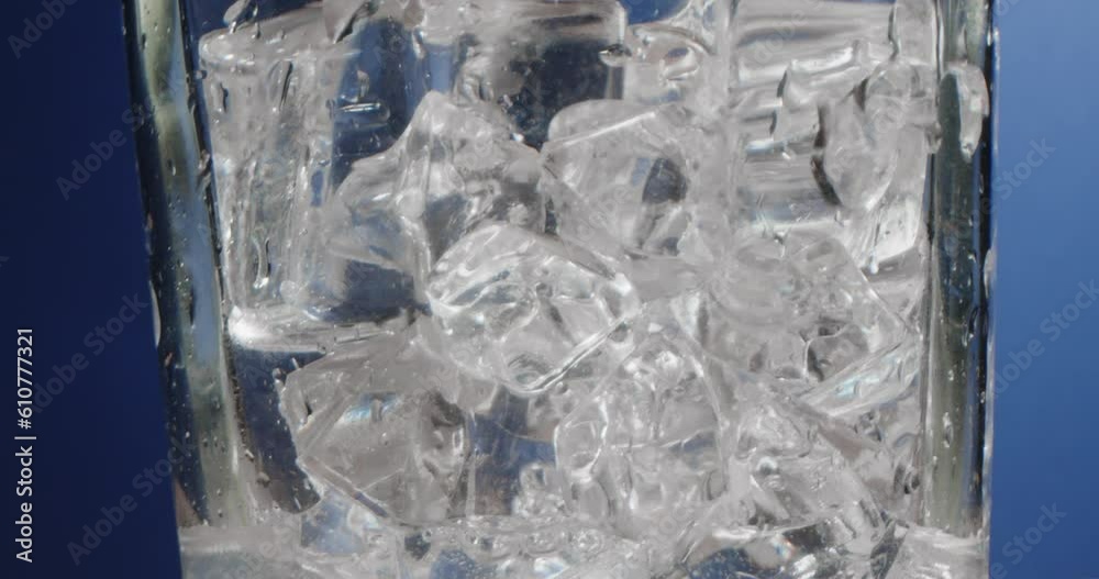 Ice cubes in a misted glass with drops of ice water close-up macro. Refreshing and chilling drink in hot weather. Blue background.