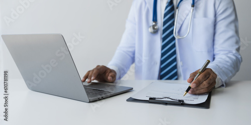 Doctor or researcher typing and looking at pill information on laptop while sitting at desk with pill bottle to analyze data and take notes on prescription. Medical and health insurance concept.