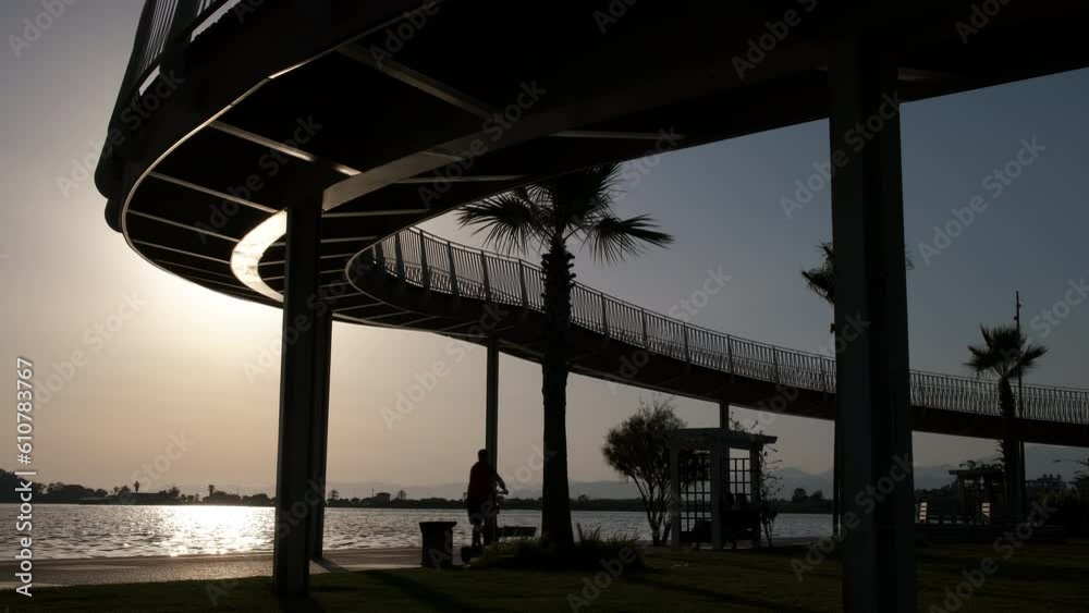 Silhouette of a man on a scooter. A man on an electric scooter rides along the embankment over the bridge. Silhouette of a man on a scooter. A man on an electric scooter rides along the embankment over the bridge.