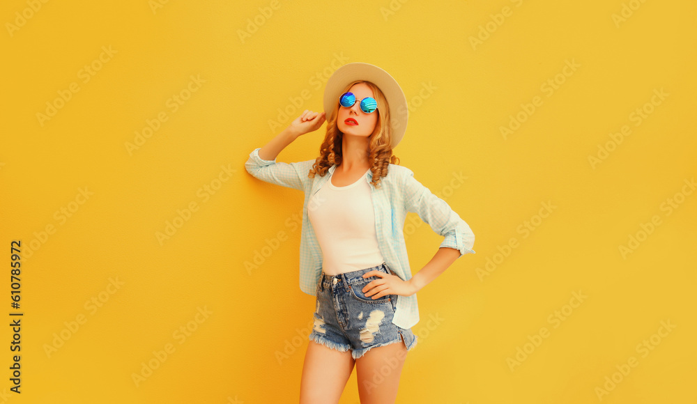 Stylish caucasian blonde young woman posing wearing straw hat, shorts and shirt on yellow background Stylish caucasian blonde young woman posing wearing straw hat, shorts and shirt on yellow background