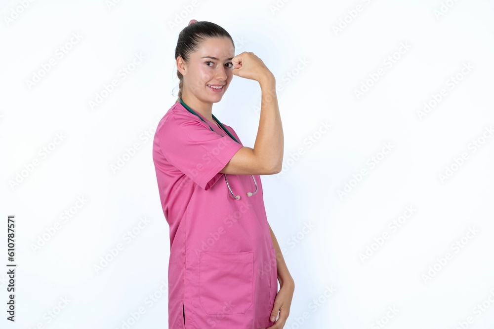 young caucasian doctor woman wearing pink uniform over white background , showing muscles after workout. Health and strength concept. young caucasian doctor woman wearing pink uniform over white background , showing muscles after workout. Health and strength concept.