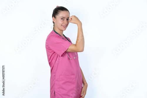 young caucasian doctor woman wearing pink uniform over white background    showing muscles after workout. Health and strength concept.
