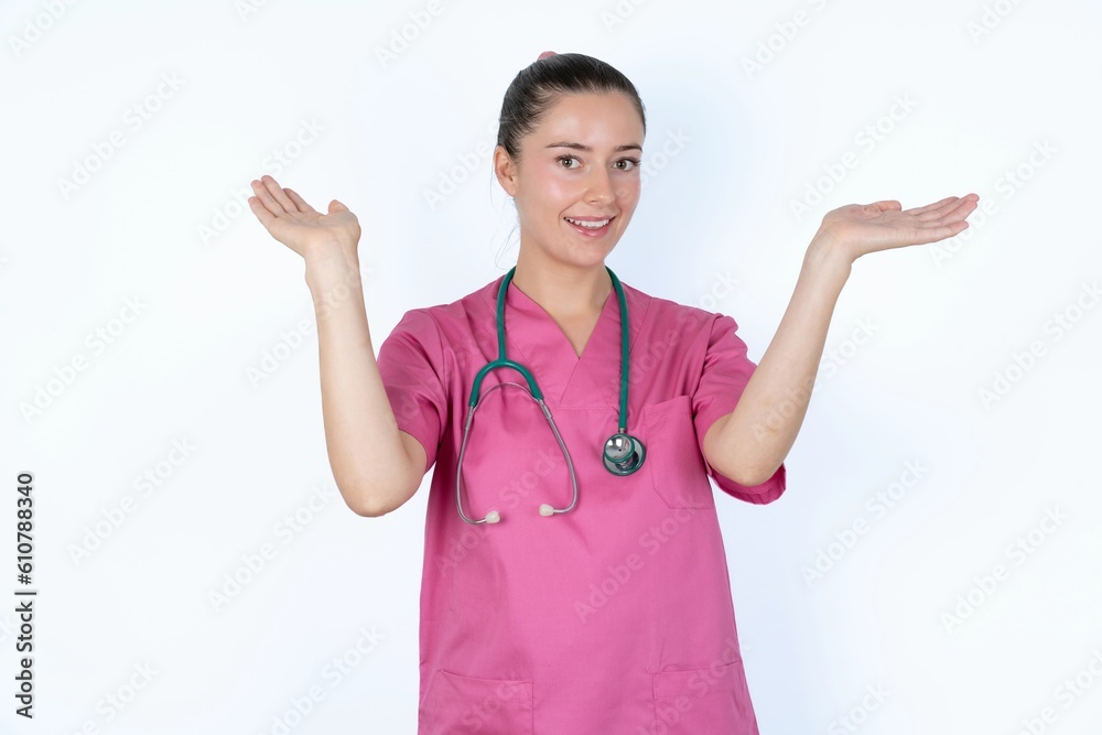 Cheerful young caucasian doctor woman wearing pink uniform over white background making a welcome gesture raising arms over head.