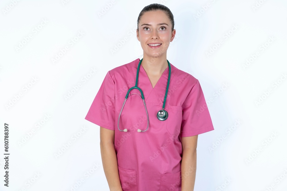Surprised young caucasian doctor woman wearing pink uniform over white background , shrugs shoulders, looking sideways, being happy and excited. Sudden reactions concept. Surprised young caucasian doctor woman wearing pink uniform over white background , shrugs shoulders, looking sideways, being happy and excited. Sudden reactions concept.