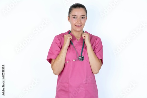 Portrait of desperate and shocked young caucasian doctor woman wearing pink uniform over white background looking panic, holding hands near face, with mouth wide open.