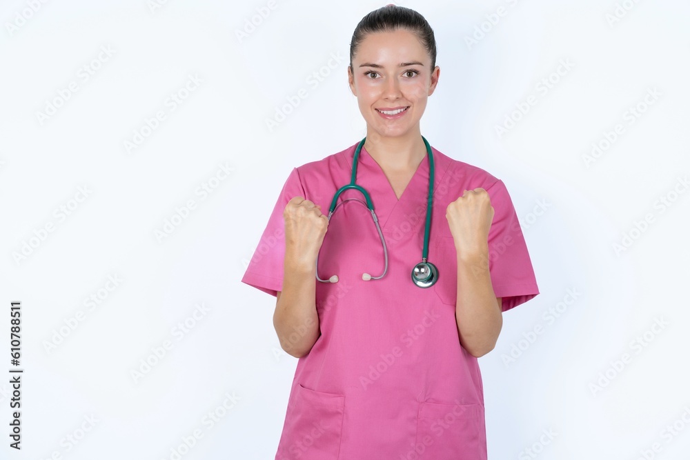 Joyful excited lucky young caucasian doctor woman wearing pink uniform over white background cheering, celebrating success, screaming yes with clenched fists Joyful excited lucky young caucasian doctor woman wearing pink uniform over white background cheering, celebrating success, screaming yes with clenched fists