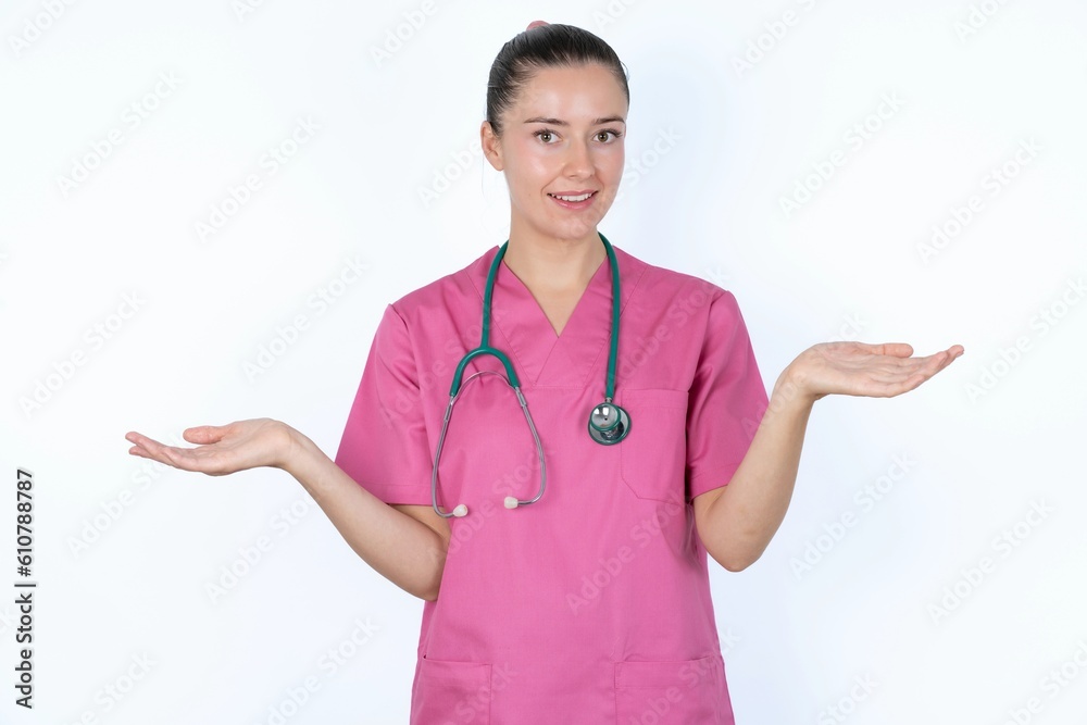So what? Portrait of arrogant young caucasian doctor woman wearing pink uniform over white background shrugging hands sideways smiling gasping indifferent, telling something obvious. So what? Portrait of arrogant young caucasian doctor woman wearing pink uniform over white background shrugging hands sideways smiling gasping indifferent, telling something obvious.