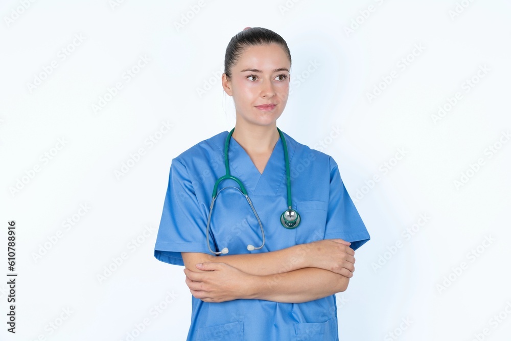Pleased young caucasian doctor woman wearing medical uniform over white background keeps hands crossed over chest looks happily aside Pleased young caucasian doctor woman wearing medical uniform over white background keeps hands crossed over chest looks happily aside