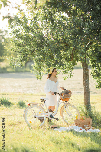 Beautiful young dark-haired woman on picnic in field. Model in stylish clothes with bicycle. Summer. © Kristina89