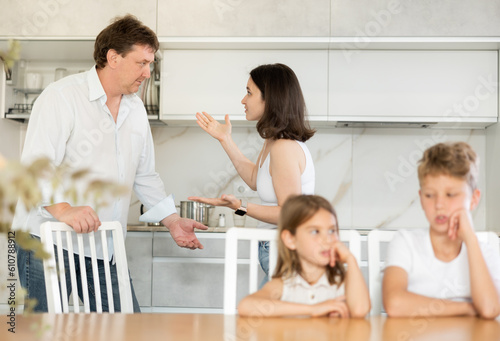 Brother and sister sitting at table in kitchen during conflict between their parents © JackF