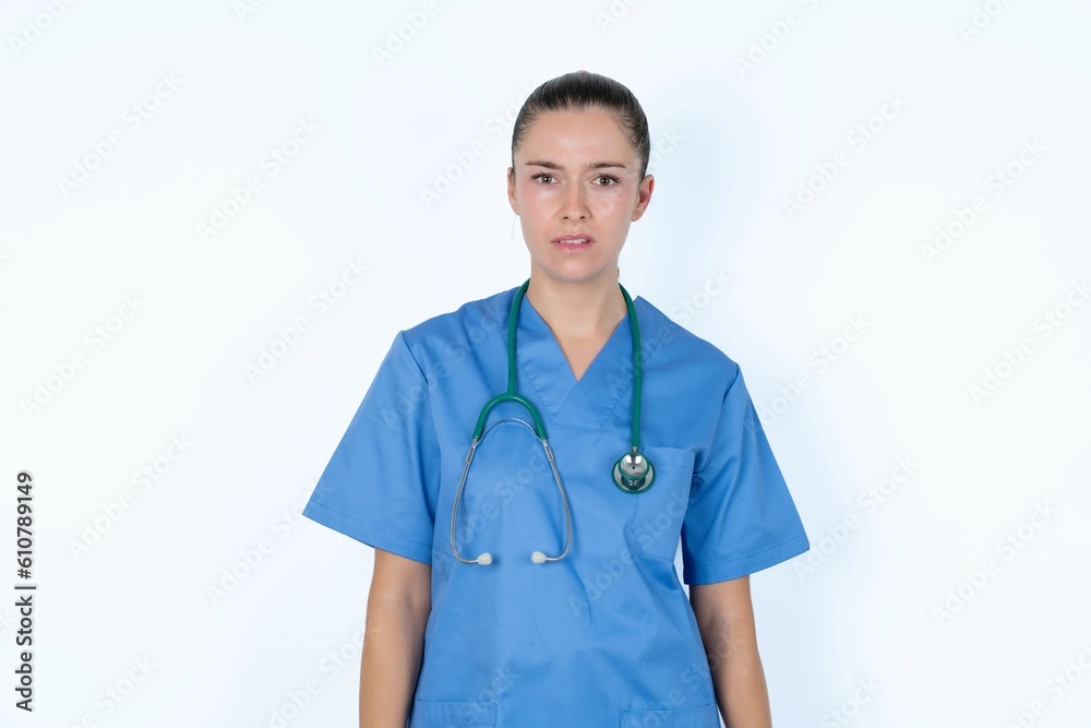 Portrait of dissatisfied young caucasian doctor woman wearing medical uniform over white background smirks face, purses lips and looks with annoyance at camera, discontent hearing something unpleasant Portrait of dissatisfied young caucasian doctor woman wearing medical uniform over white background smirks face, purses lips and looks with annoyance at camera, discontent hearing something unpleasant