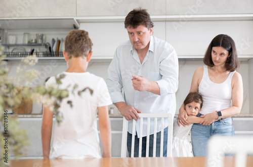 Mom and dad scold their guilty son standing in kitchen at home