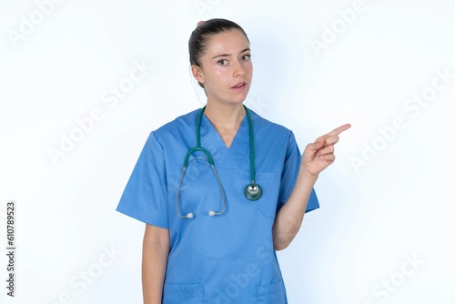 Emotive young caucasian doctor woman wearing medical uniform keeps jaw dropped from shock demonstrates amazing promo points right on blank space demonstrates big shopping sale. Advertisement